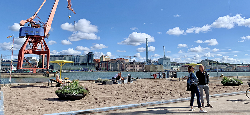 Playan på Lindholmen består av bänkar, solstolar, parasoller, sand och gröna inslag, allt med en utsikt över Lindholmens kranar och Göta älv.